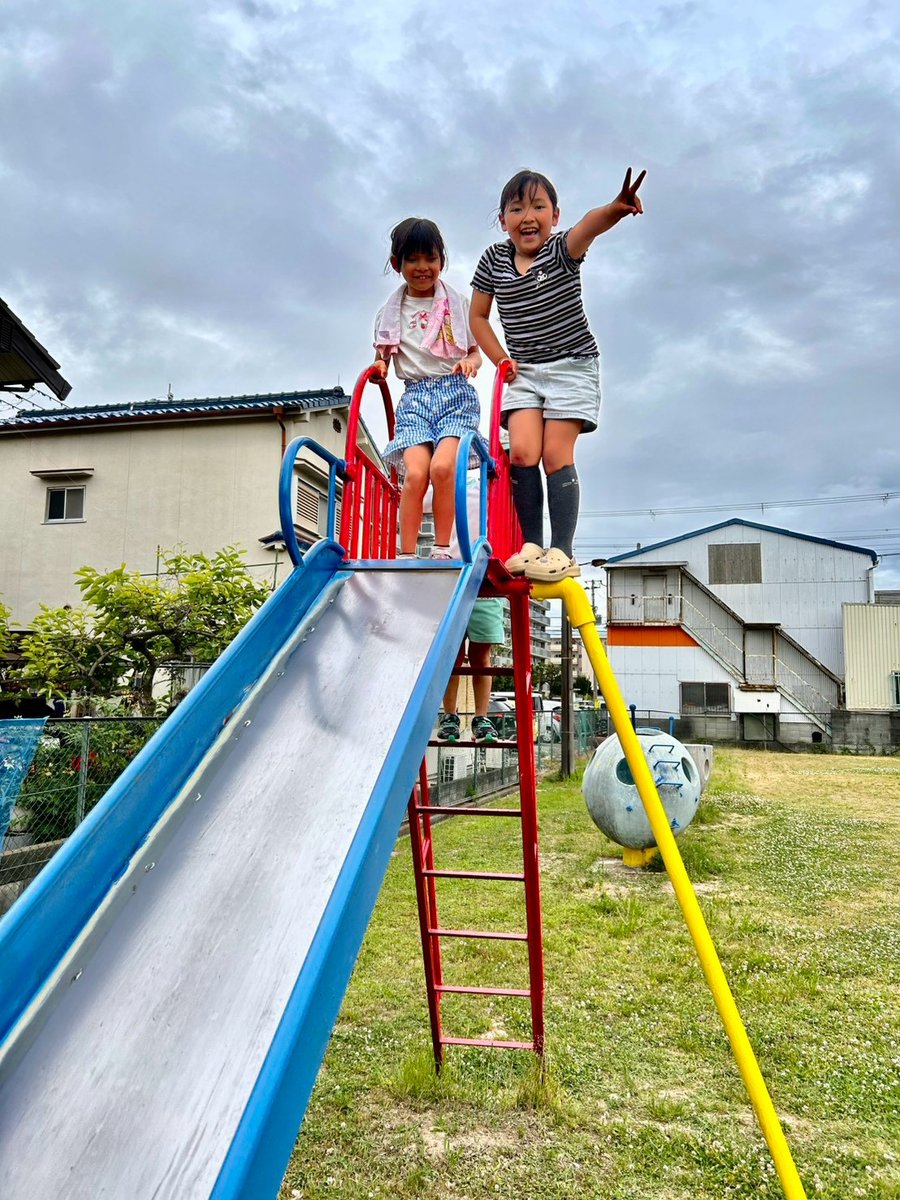 公園のすべり台の上で手を挙げる子どもたち