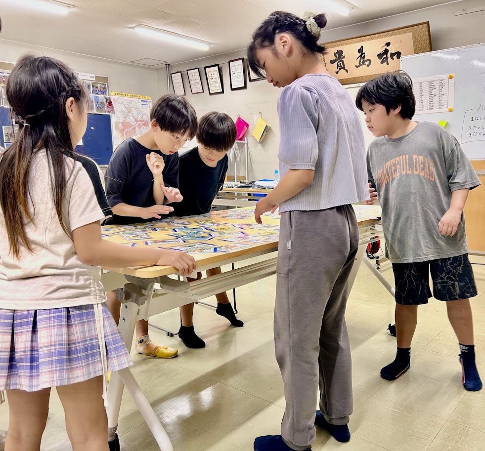 机を囲んで英語のカルタに取り組む子どもたち