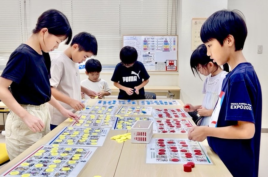 大きなカルタのシートを囲んで遊ぶ子どもたち